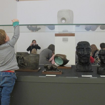 small boy stretches over gallery case and is photographed by researcher through the glass